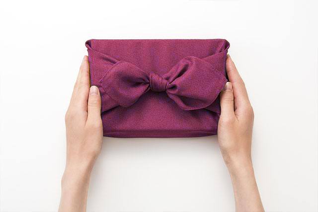 紫色の風呂敷に包んだ贈り物を差し出す女性の手