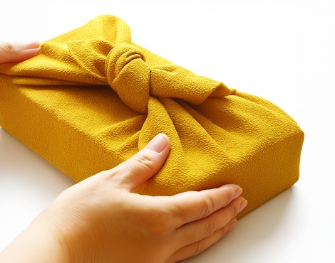 黄色の風呂敷に包まれた贈り物を渡す女性